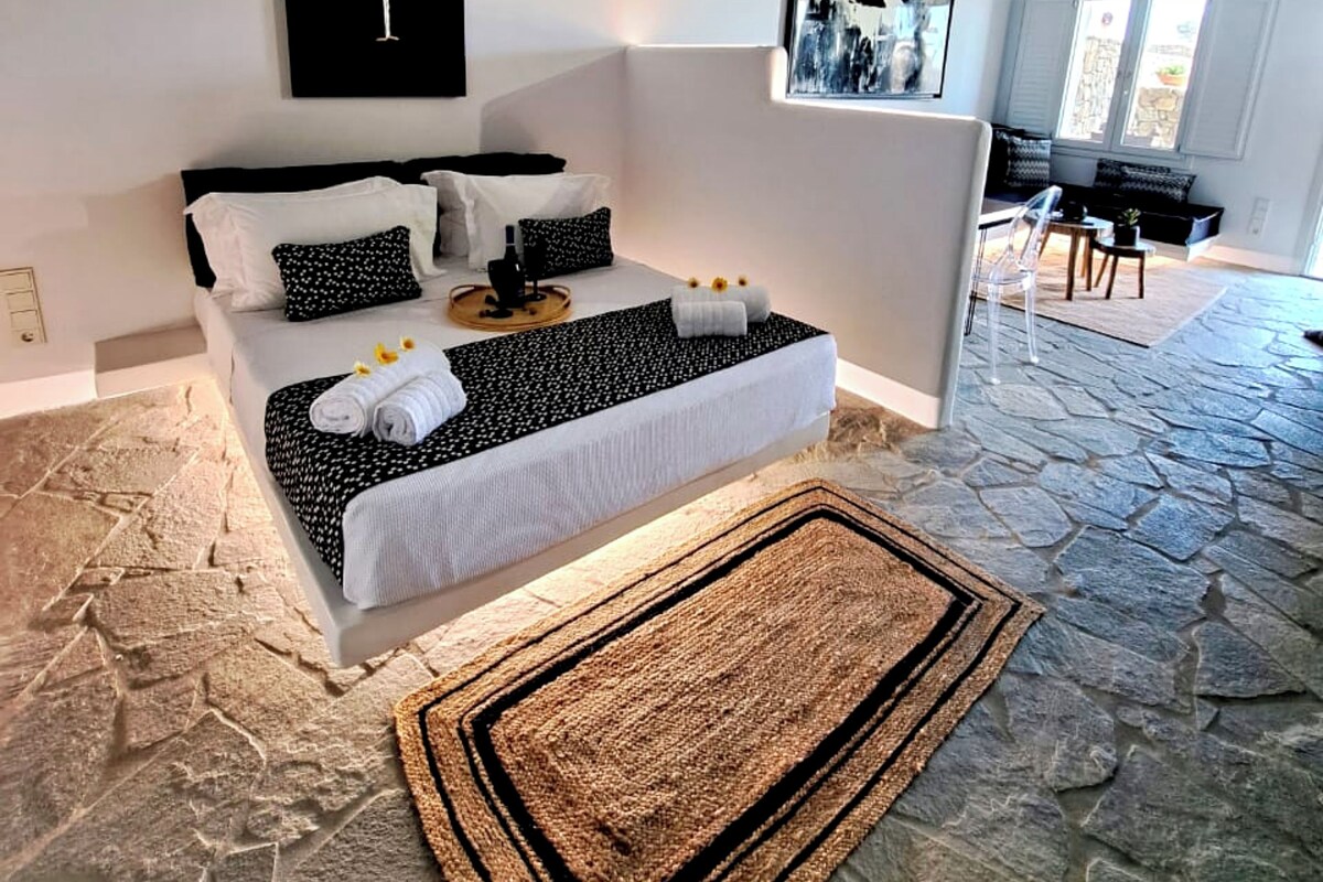 Een moderne slaapkamer met stenen vloer, een bed met wit- en zwart beddengoed, en twee abstracte kunstwerken aan de muur.
