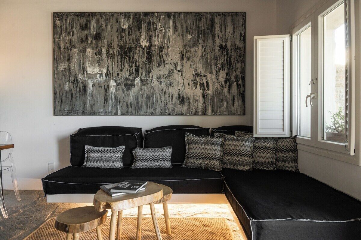 Un salon moderne avec un canapé noir, des coussins à motifs, un grand tableau abstrait et une table basse en bois.