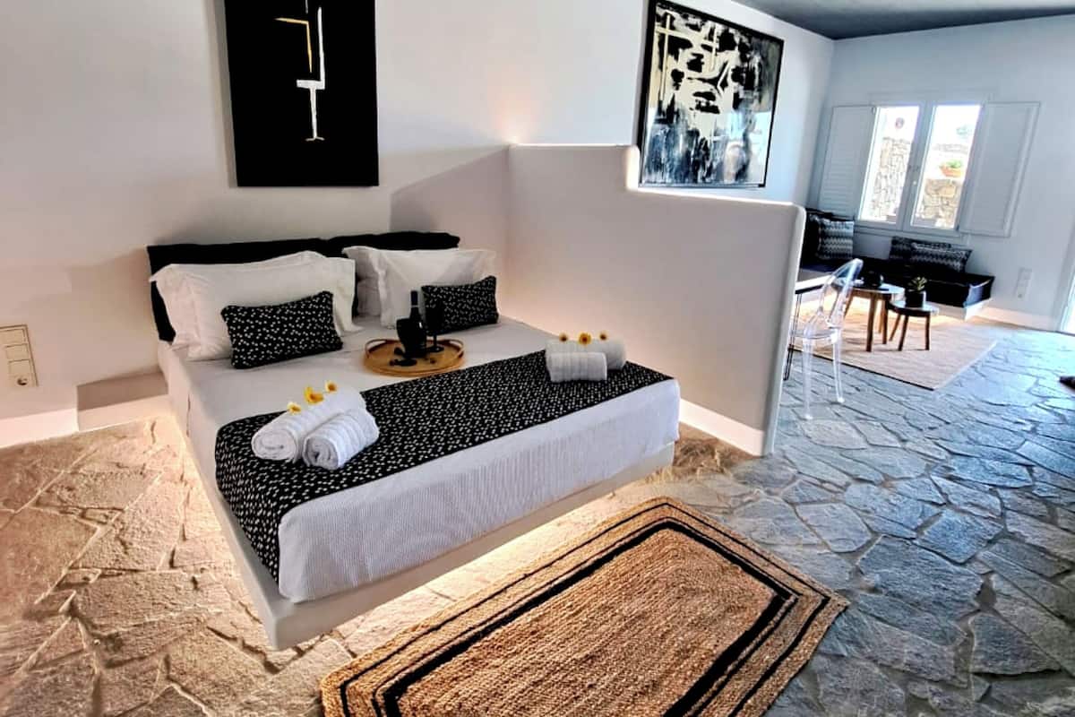 Ein modernes Schlafzimmer mit Steinboden, einem Bett mit weißer und schwarzer Bettwäsche sowie zwei abstrakten Wandbildern.