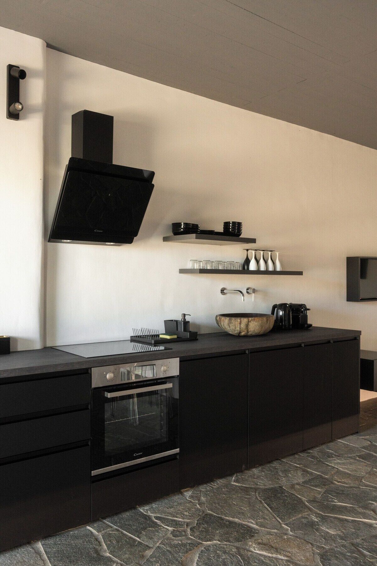 A modern kitchen with a built-in oven, a large island with a sink, and a flat-screen TV mounted on the wall.