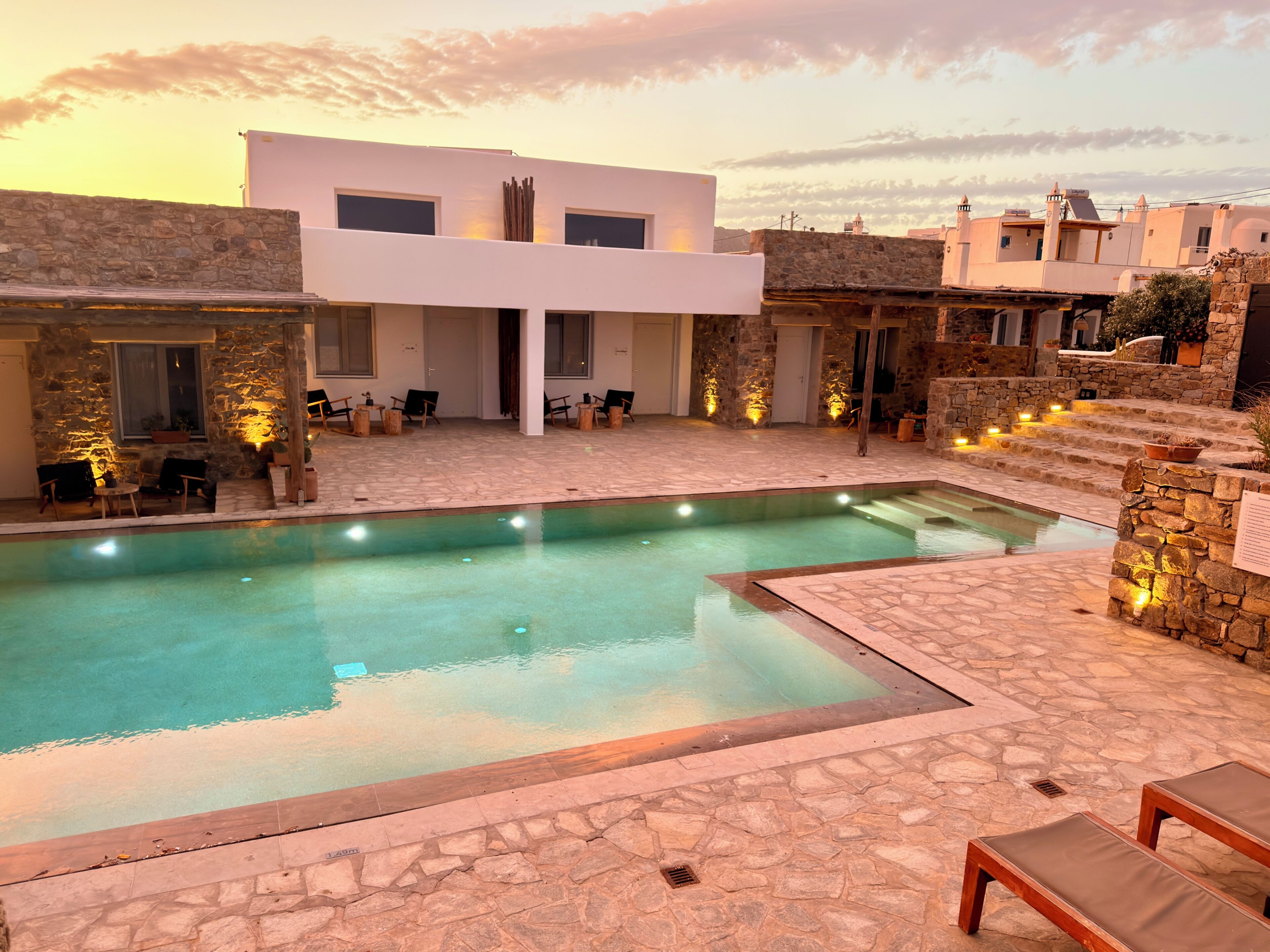 A pool area with stone flooring, a modern building with large windows, and outdoor seating.