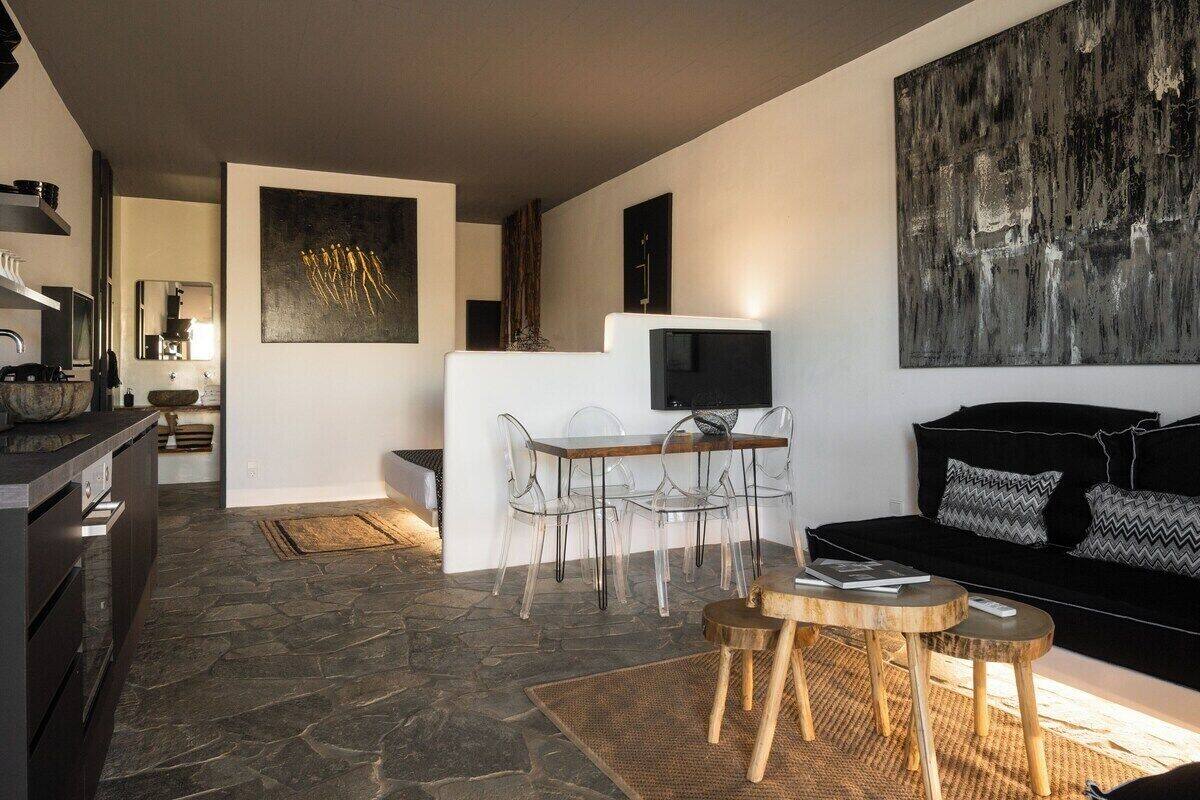 Ein modernes Wohnzimmer mit einer schwarzen Couch, einem Essbereich mit klaren Stühlen und einem Steinboden.