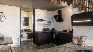 A modern kitchen with dark cabinetry, a stone countertop, and a large island with a bowl sink. - Mykonos Dot - Art Homes (Ano Mera)