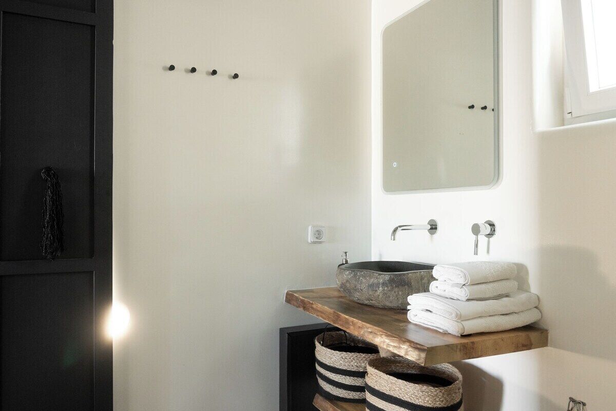 Un baño con tocador de madera, un lavabo redondo y un espejo encima. Hay toallas apiladas sobre el tocador y cestas debajo.