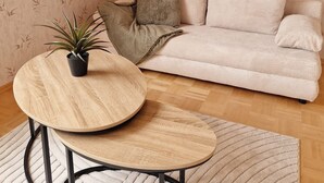 Ein Wohnzimmer mit einem beigen Sofa, einem runden Holztisch und einer Zimmerpflanze.