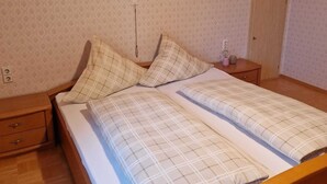 Ein Schlafzimmer mit Holzbalkendecke, zwei Betten mit Karo-Bettwäsche, einem Nachttisch, einer Kommode und einer Tür.