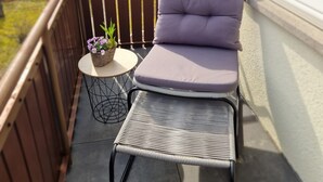Ein Balkon mit gepolstertem Stuhl und einem Tisch mit einer Pflanze.