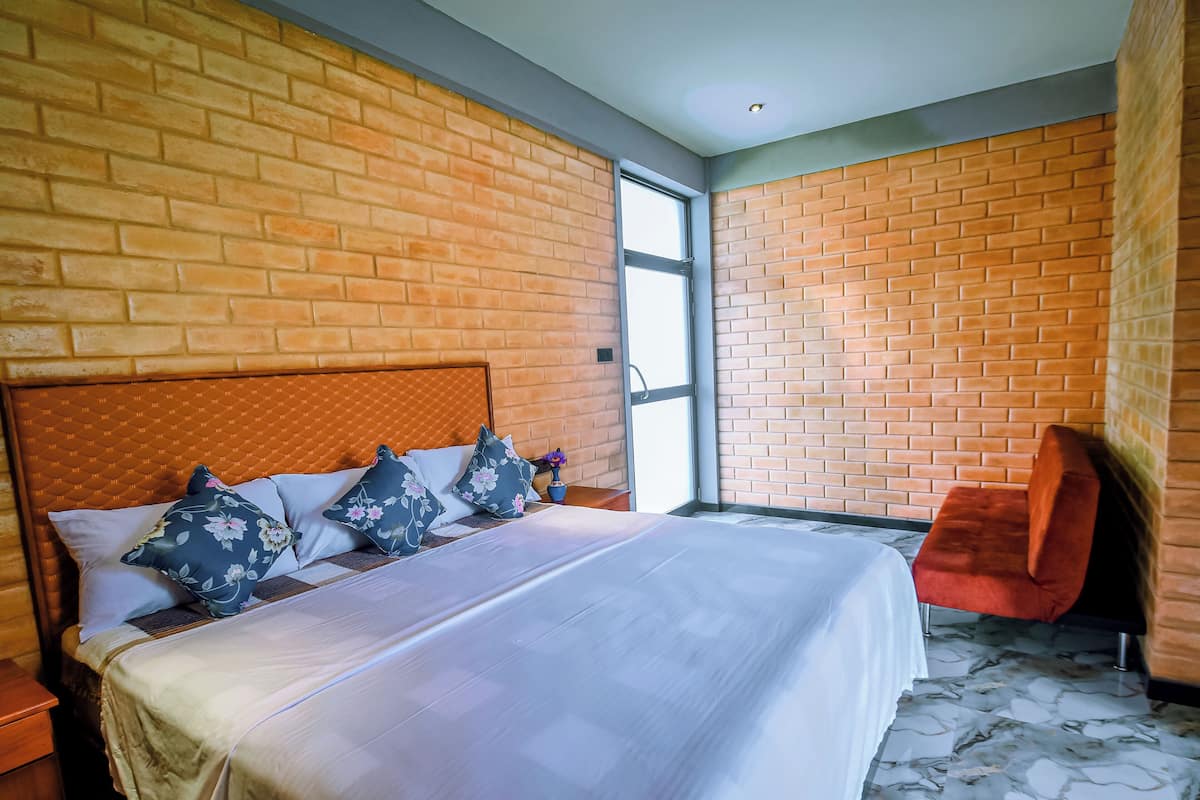 Ein Hotelzimmer mit einer Wand im Backsteinmuster, einem Bett mit Blumenkissen, einem roten Sessel und einem Marmorboden.