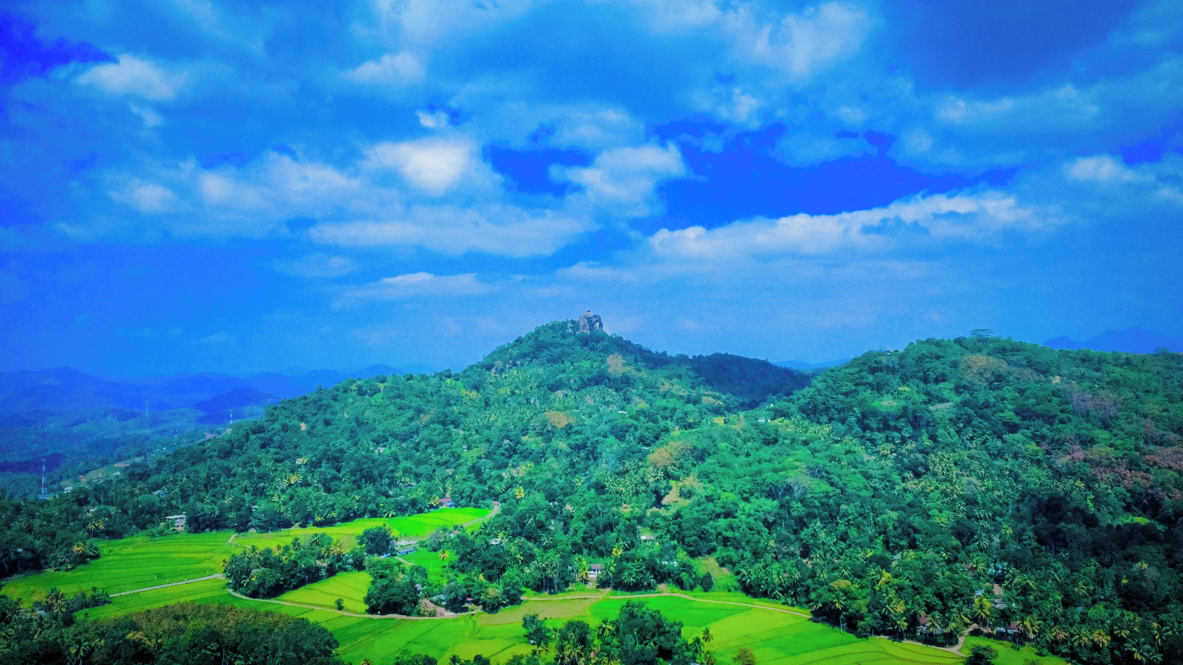 A lush green landscape with terraced fields and a prominent hill with a structure on top.