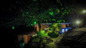 A nighttime view of a building with illuminated windows and a garden area with rocks and plants. - Rocksana Fortress Yoga & Retreat (Mawanella)