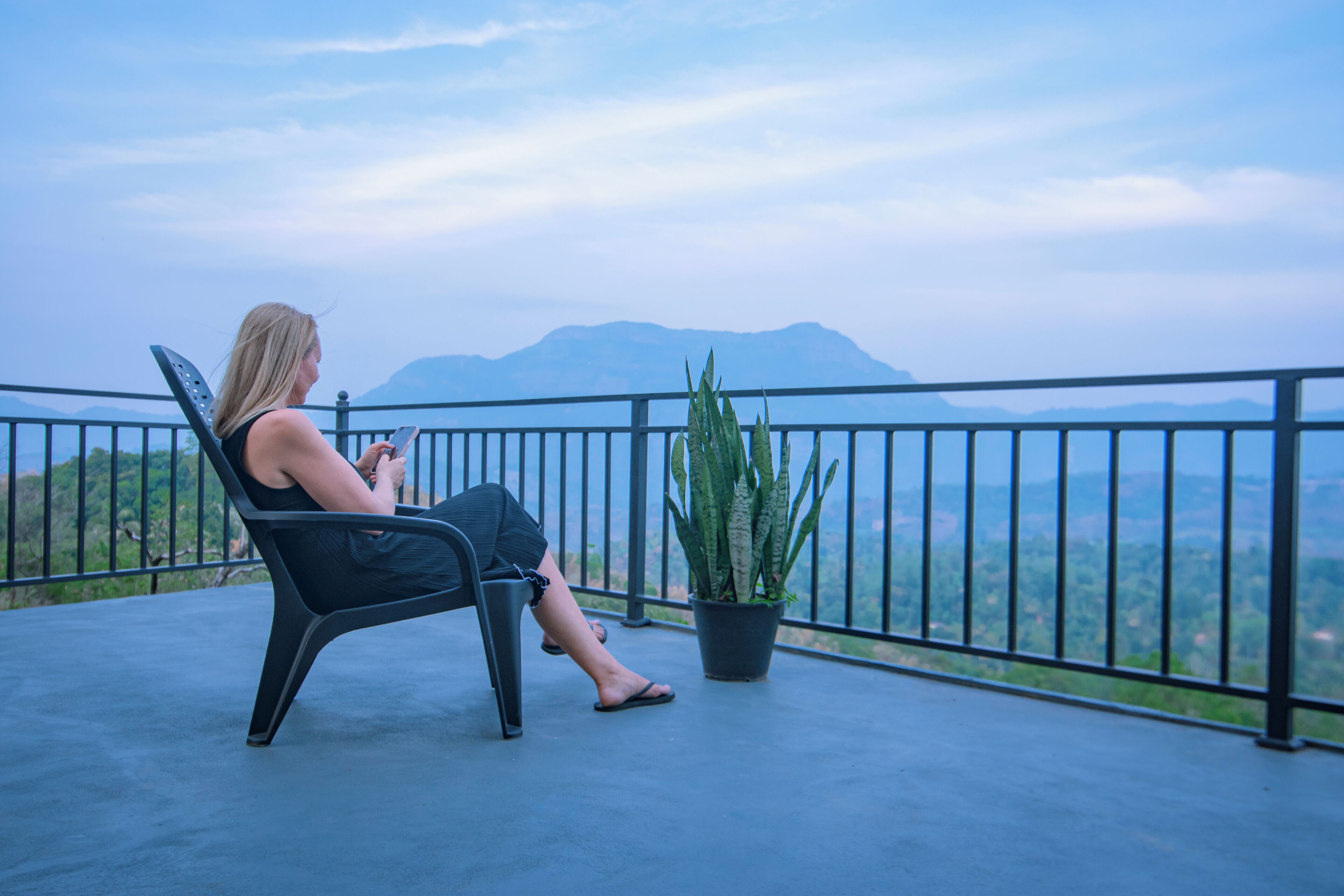 Une personne assise sur une chaise, sur un balcon, avec vue sur les montagnes.