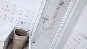 Ein modernes Badezimmer mit einer einachigen Duschkabine, einem weißen Waschbecken und einem beige gefärbten Mülleimer.
