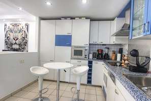 A modern kitchen with white cabinets, a microwave, a coffee maker, and a sink. There are two white bar stools and a tiger painting on the wall. - Beachside Apartment With Jacuzzi & Pool (Marbella)