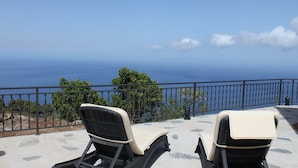 Zwei Liegestühle mit Blick auf ein Meer von einem Balkon aus.