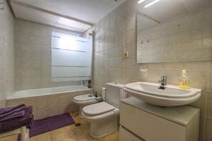Une salle de bain avec une baignoire, deux toilettes, un lavabo et un miroir.