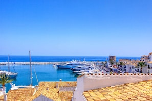 A coastal marina with yachts docked, a clear blue sky, and buildings with terracotta roofs. - Puerto Banus Apartment for 8 (Marbella)