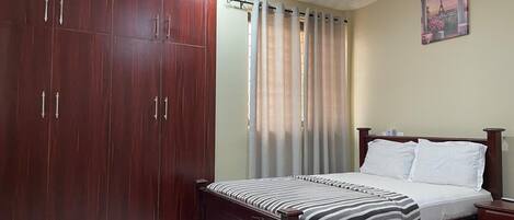 A bedroom with a bed, a wardrobe, a ceiling fan, and a painting on the wall.