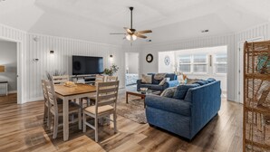 Een ruime woonkamer met een houten eettafel, een blauwe bank en een plafondventilator.