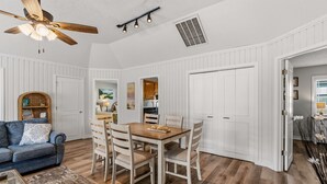 Een eetgedeelte met een houten tafel en stoelen, een plafondventilator en witte wandpanelen.