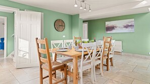 A dining area with a wooden table and chairs, a clock on the wall, and a painting above the table.