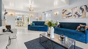 A modern living room with a blue sofa, a coffee table, and a vase with flowers. There is a dining area in the background with a table and chairs. - Tackley House - pet friendly near Oxford (Near Oxford)