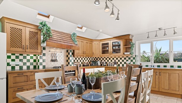 A modern kitchen with wooden cabinets, a dining table set for four, and a large window providing natural light. - Tackley House - pet friendly near Oxford (Near Oxford)