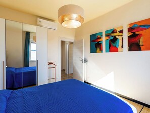 Een hotelkamer met een groot bed, een kledingkast, een spiegel en drie kleurrijke schilderijen aan de muur.