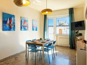 A dining area with a table set for four, blue chairs, and a window with curtains.