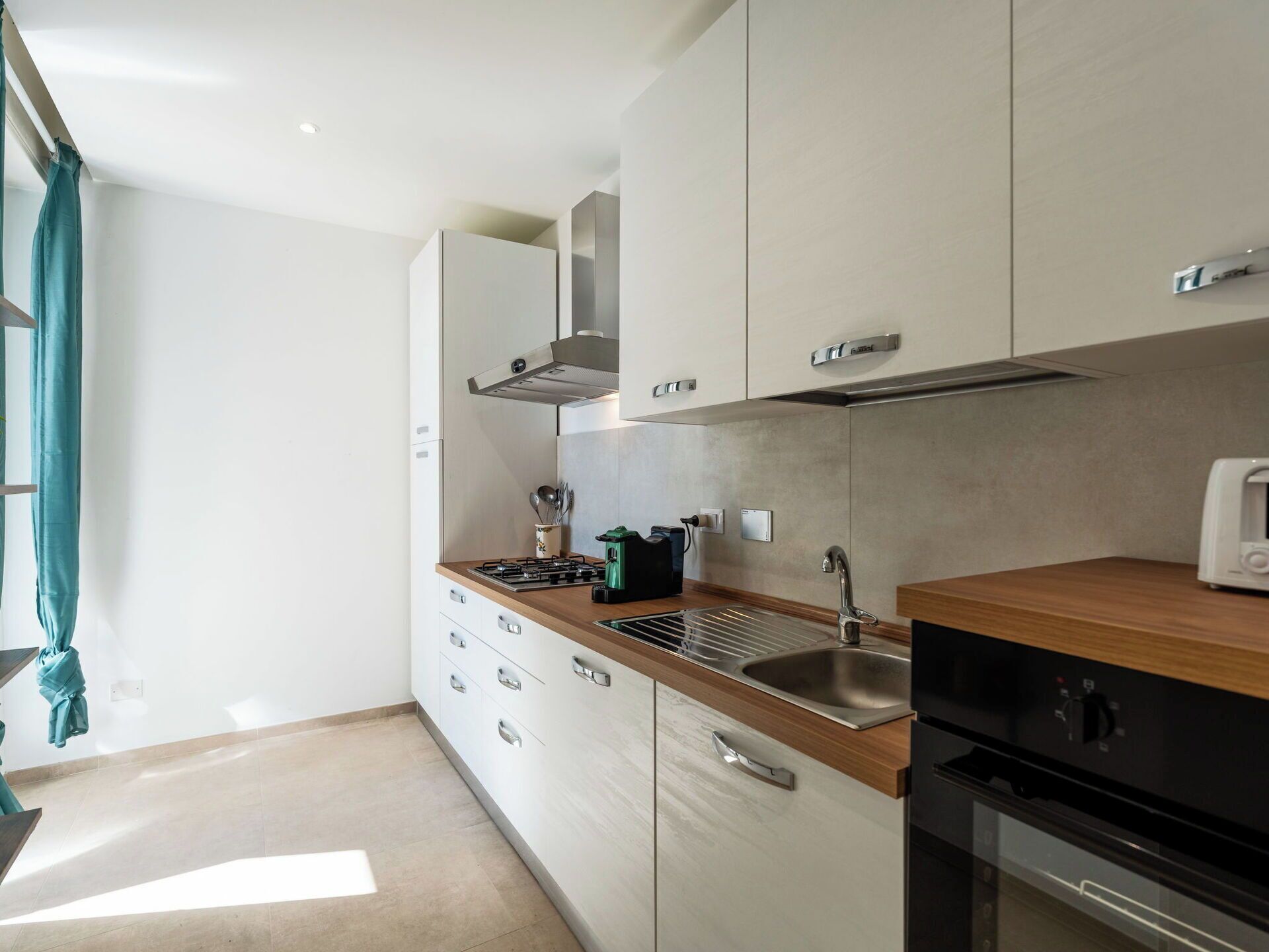 A modern kitchen with white cabinets, a wooden countertop, a stainless steel sink, and a black oven.