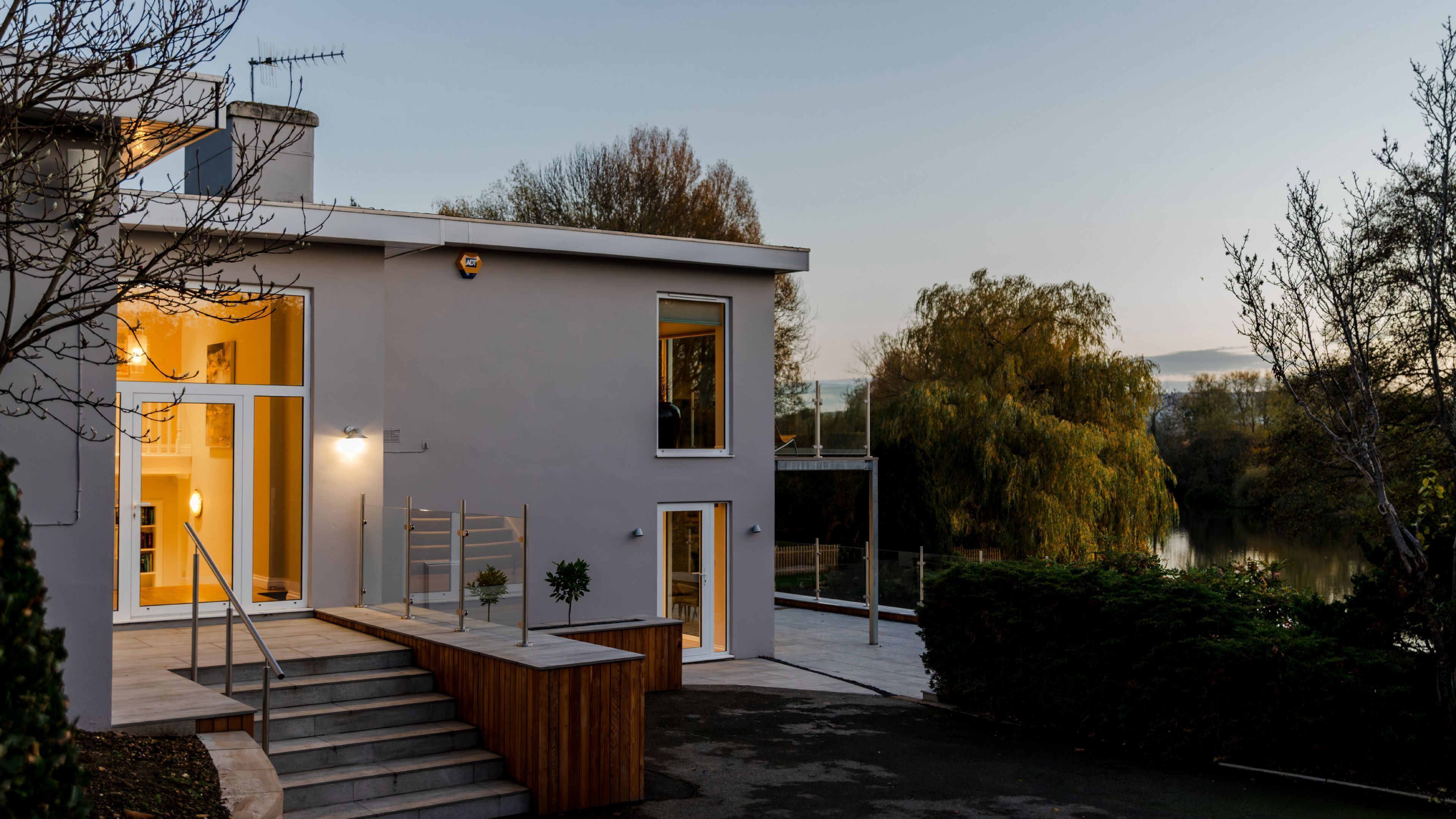 Une maison moderne avec un escalier menant à l’entrée, un petit jardin et une vue sur un lac.