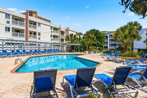 A swimming pool with lounge chairs, a brick pool deck, and a multi-story building with balconies. - Pelicans Landing 213 3 BR Beach/Pool (Myrtle Beach)
