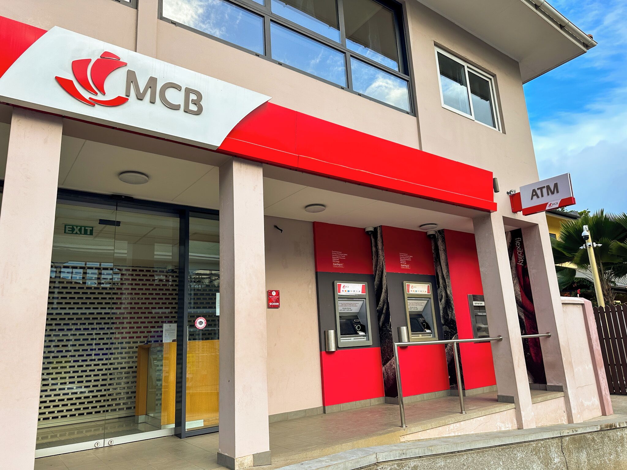 A MCB bank with an ATM, glass doors, and a red and white facade.