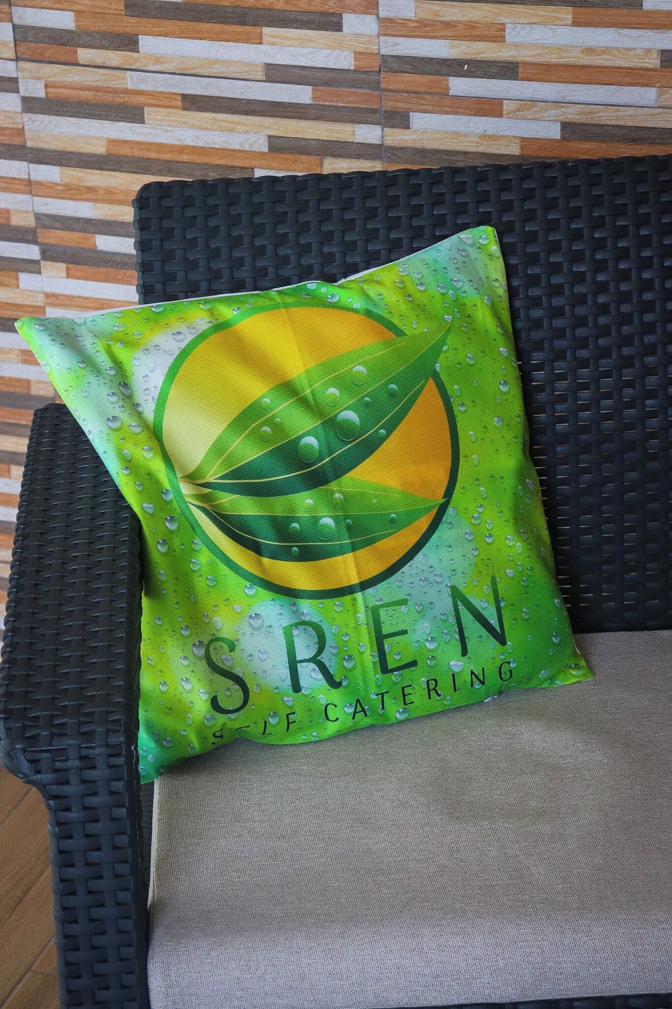 A green cushion with a leaf design and the text 'SREN Catering' on a wicker chair.