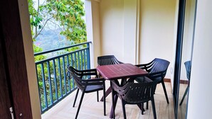 Un balcón con mesa y sillas, vistas a la vegetación y una puerta.
