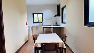 A narrow hallway leading to a kitchen with a dining table and chairs, a window, and a tiled backsplash.