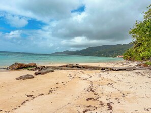 Una playa con agua cristalina, formaciones rocosas y una cadena montañosa al fondo.