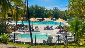 Un espace piscine aménagé avec des chaises longues, des parasols et des palmiers.