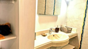 Une salle de bain avec un lavabo, un miroir et des étagères où sont rangées des chaussures.