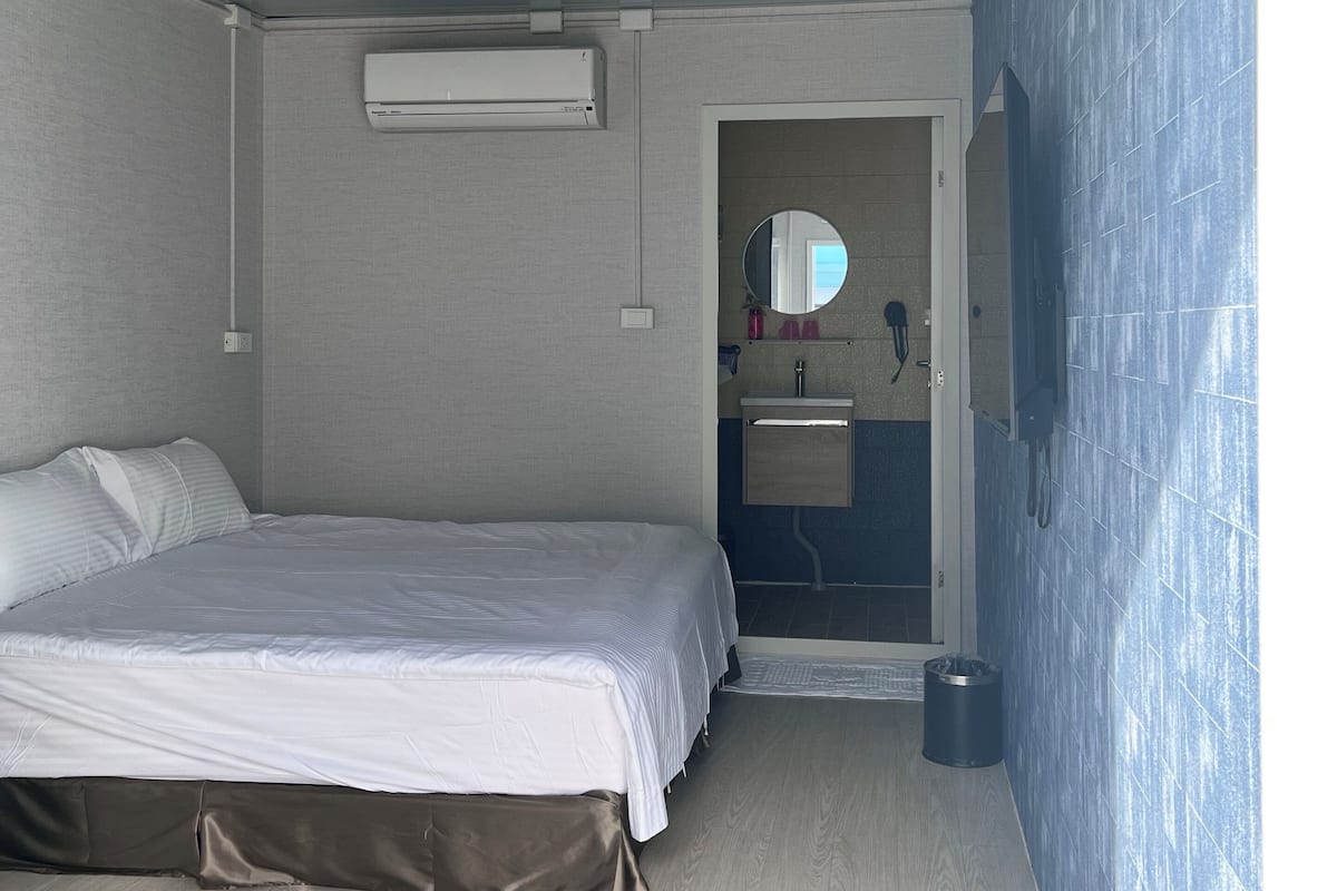 Un dormitorio con cama, aire acondicionado, espejo y baño visible a través de una puerta abierta.