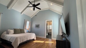 Ein Schlafzimmer mit einem Bett, einem Deckenventilator, Holzboden und einer Tür zu einem Badezimmer.
