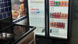 Two refrigerated beverage dispensers labeled 'POLOFRIO' with various drinks inside, a tiled backsplash, and a kitchen counter with a sink and cabinets. - Hotel Hallas (Betim)