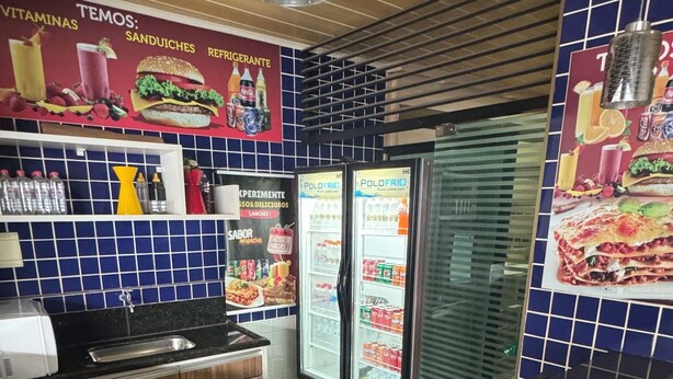 A restaurant interior with a marble counter, two refrigerators, and a tiled wall with food advertisements. - Hotel Hallas (Betim)
