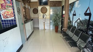 A hotel lobby with a reception desk, a red carpet with a logo, a waiting area with chairs, and a large window with a view. - Hotel Hallas (Betim)