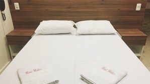 A hotel room with a wooden headboard, two white pillows, and two towels with 'Hotel Keller' embroidered on them. - Hotel Hallas (Betim)