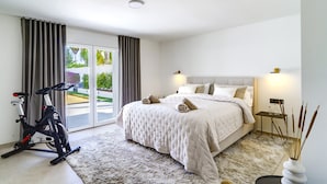 A modern bedroom with a large bed, exercise bike, and a view of the outdoors through a sliding door. - Luxury Family Villa for in Marbella (Marbella)