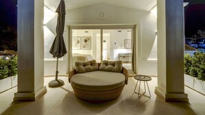 A circular wicker sofa with cushions in a well-lit outdoor area with white columns, a small round table, and a covered umbrella. - Luxury Family Villa for in Marbella (Marbella)