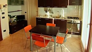 A modern kitchen with dark cabinets, a dining table with orange chairs, and a TV mounted on the wall. - Dietro la piazza (Marostica)