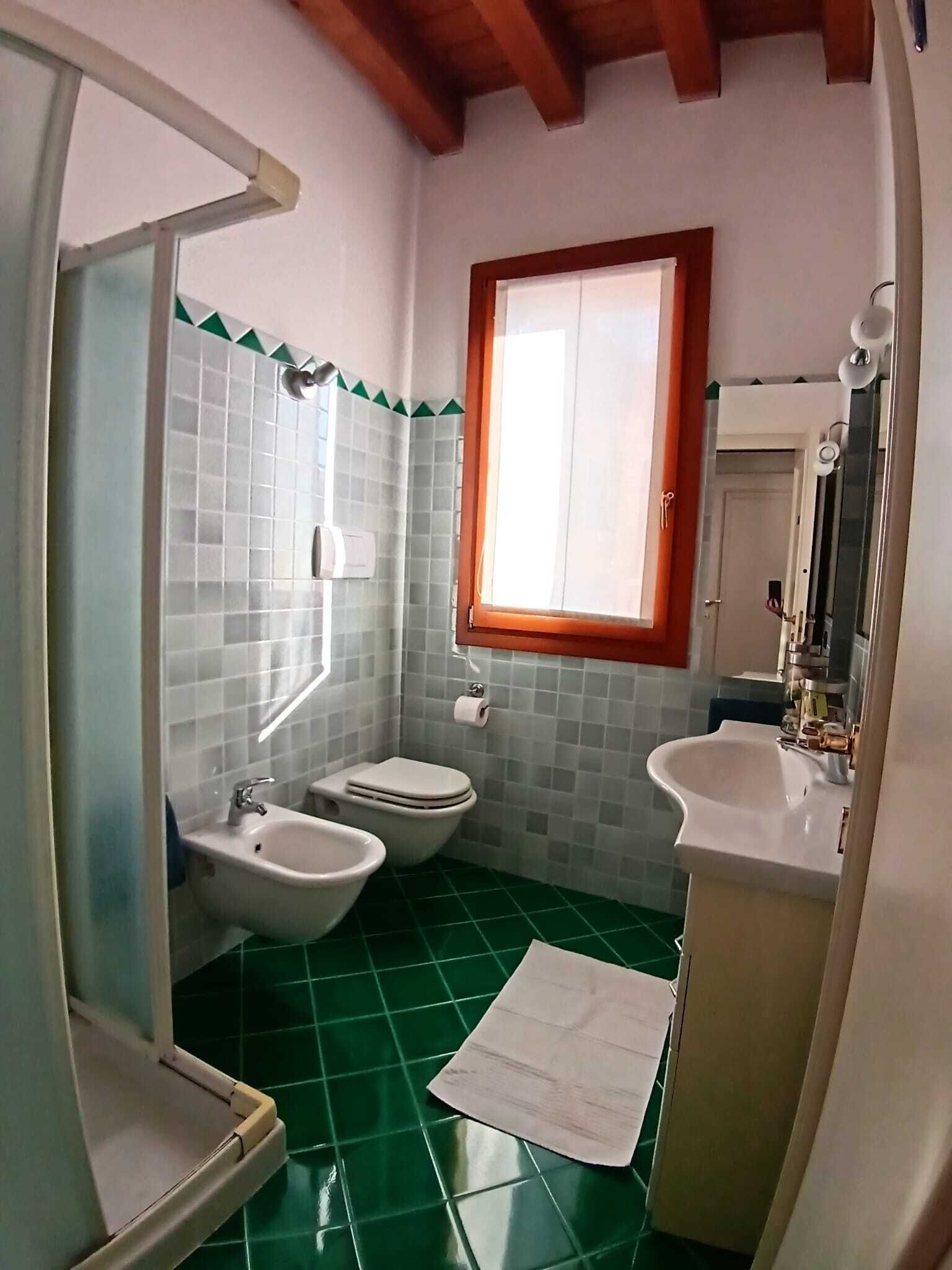 A bathroom with a green tiled floor, a white sink, a bidet, and a toilet.