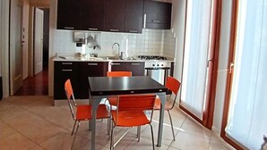 A compact kitchen with dark cabinets, a gas stove, and a dining area with orange chairs. - Dietro la piazza (Marostica)