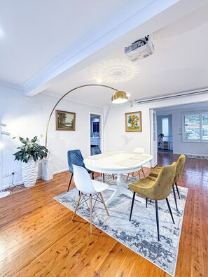 A modern dining area with a round table, white chairs, a patterned rug, and a ceiling-mounted projector. - Spacious 4BR Home with Swimming Pool | Free Parking (Picnic Point)